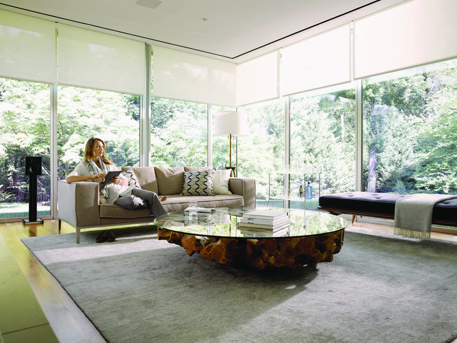 Woman sitting in a living room with Savant motorized shades across two walls of windows.
