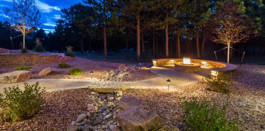 A backyard and firepit area illuminated by landscape lighting.