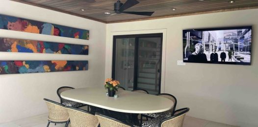 An outdoor covered patio with a modern entertainment setup, featuring a wall-mounted TV on the right.