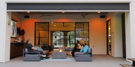 People relaxing in an outdoor area with a TV. An outdoor screen by Screen Innovations is partially lowered.