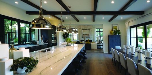 A kitchen and living area features modern recessed lighting and pendants over a large island.