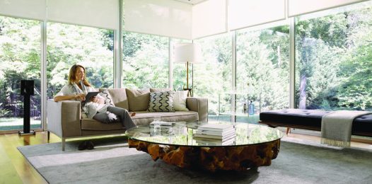 Woman sitting in a living room with Savant motorized shades across two walls of windows.