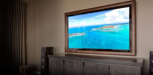 A Séura mirror TV above a counter and cabinet doors, with speakers on either side of the cabinets.