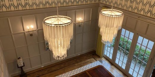two chandeliers hanging from the ceiling above a wooden table and wall of windows